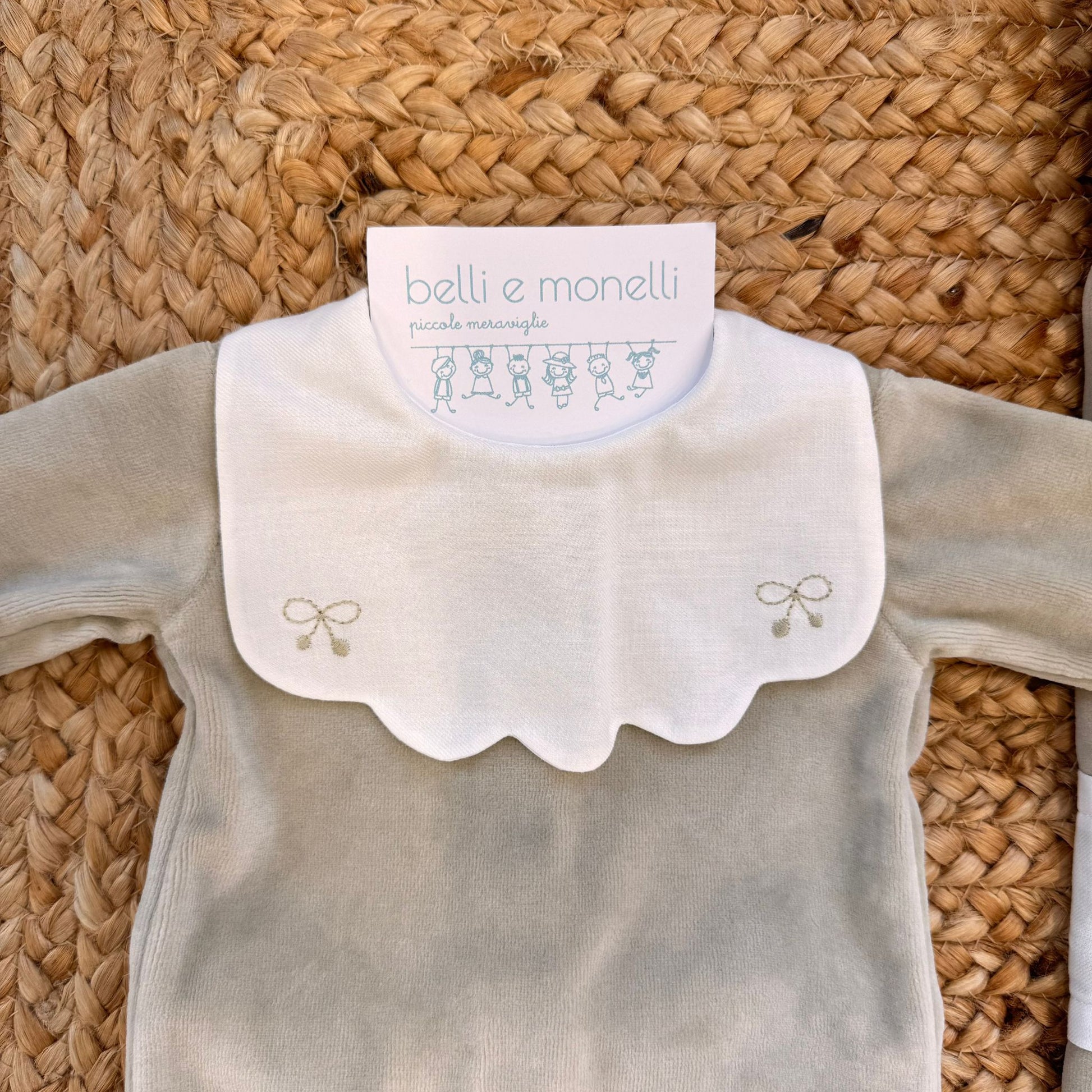Dettaglio tutina due pezzi beige con colletto bianco e ricami a fiocchetto.