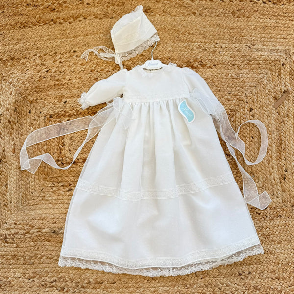 Dettaglio del tessuto a piccoli pois dell'abito battesimo neonata, con ricami floreali bianchi e bordo in pizzo smerlato.
