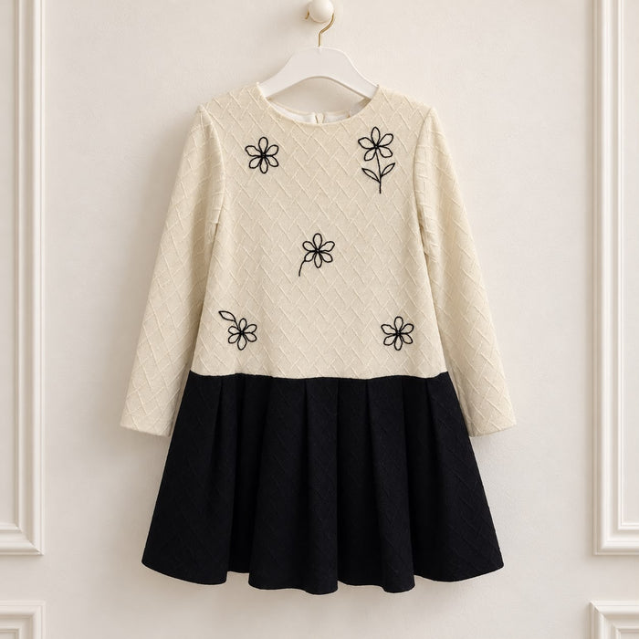 Abito elegante bambina panna e nero con fiori ricamati neri, corpetto lavorato a rombi, maniche lunghe e gonna nera a pieghe.