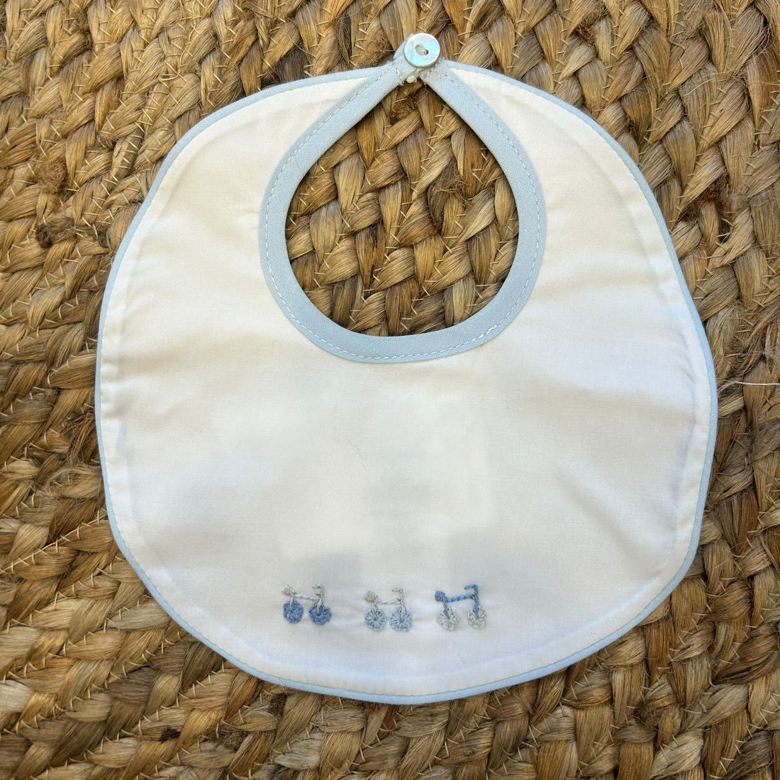 Bavaglino neonato con bordino azzurro e ricamo bici in cotone bianco.