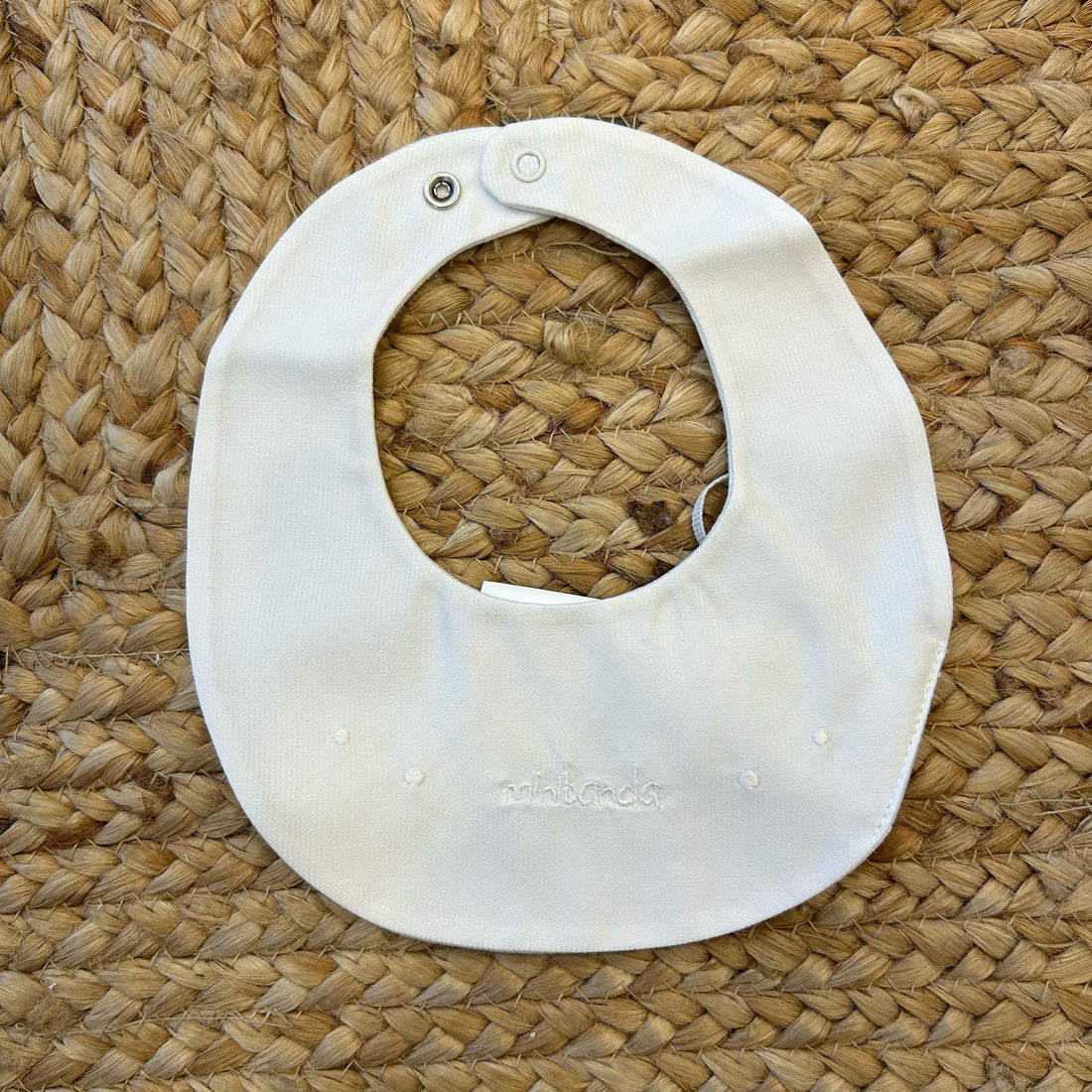 Bavaglino neonato panna con ricamo bianco “ninnanda” e chiusura a clip.