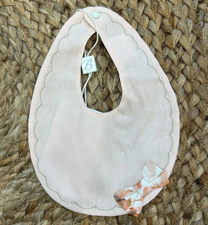 Bavaglino neonata rosa pesca in lino con bordo smerlato e fiocchetto fantasia.