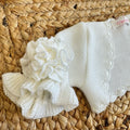 Dettaglio maniche con balze e fiore applicato sul coprispalle in maglia avorio per bambina.