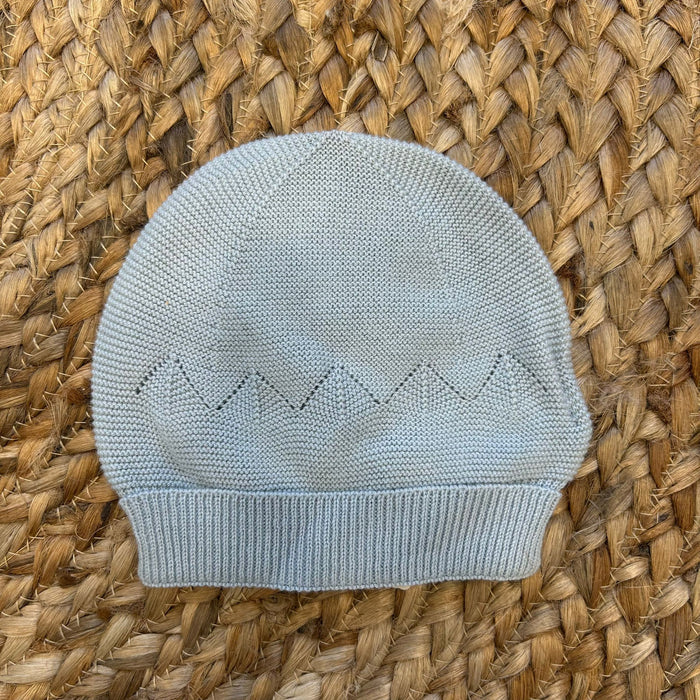 Cappellino in maglia azzurro polvere per neonato con lavorazione traforata e bordo a costine.