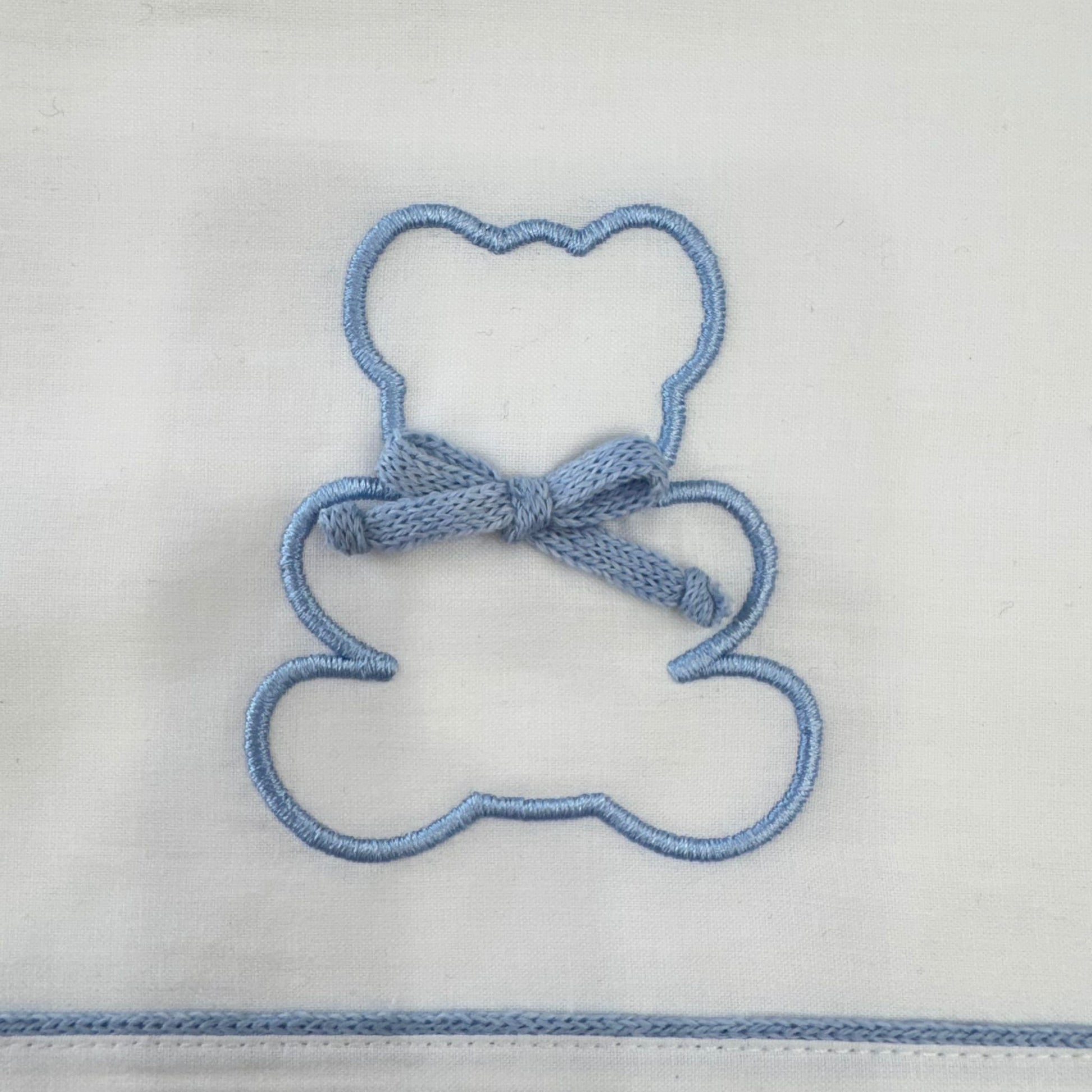Dettaglio ricamo orsetto con fiocco azzurro su lenzuolino bianco in cotone per culla neonato