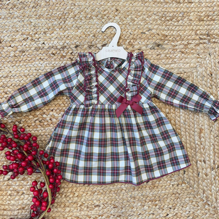 Abito natalizio per bimba in tessuto scozzese beige, bordeaux e verde con balze frontali e fiocco bordeaux laterale.