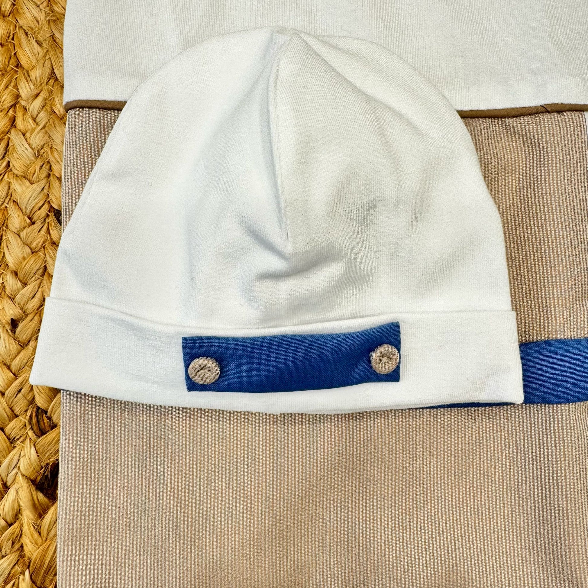 Cappellino in cotone con applicazioni in tessuto, perfettamente abbinato alla tutina per un look armonioso e sofisticato.

