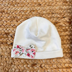 Cappellino neonato in caldo cotone con fiocco floreale e charm a cuore.

