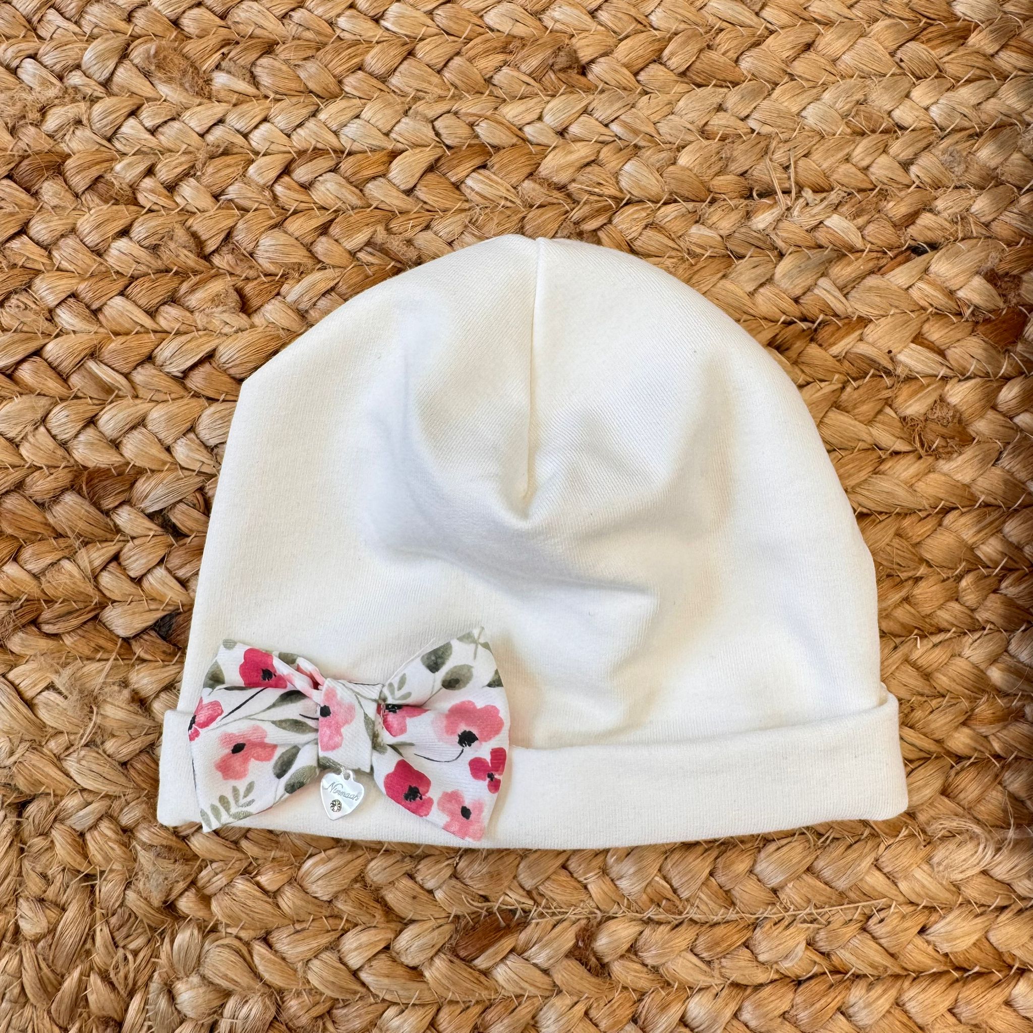 Cappellino neonato in caldo cotone con fiocco floreale e charm a cuore.


