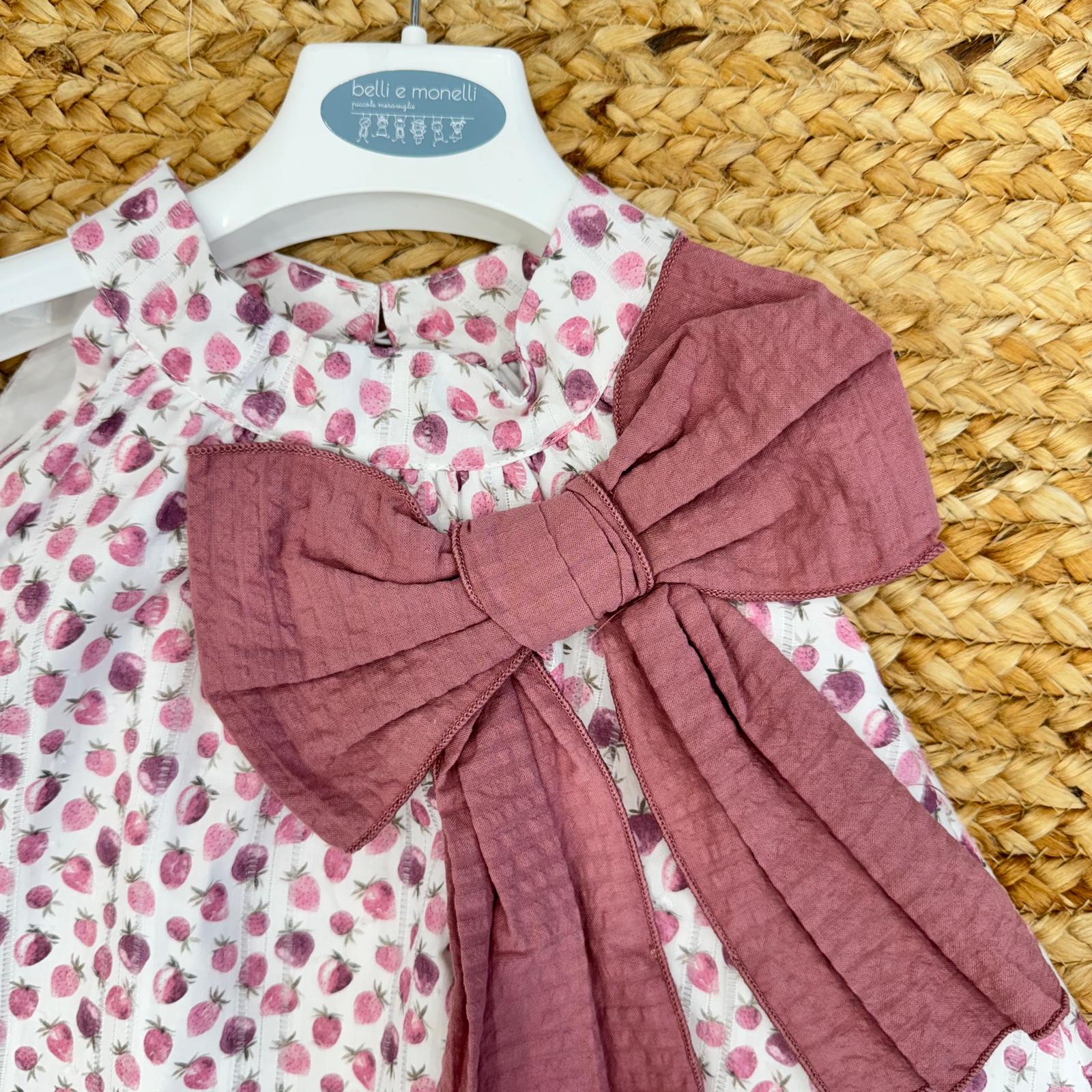 Primo piano del fiocco maxi color malva applicato sull'abito con fragoline, dettaglio raffinato e romantico.