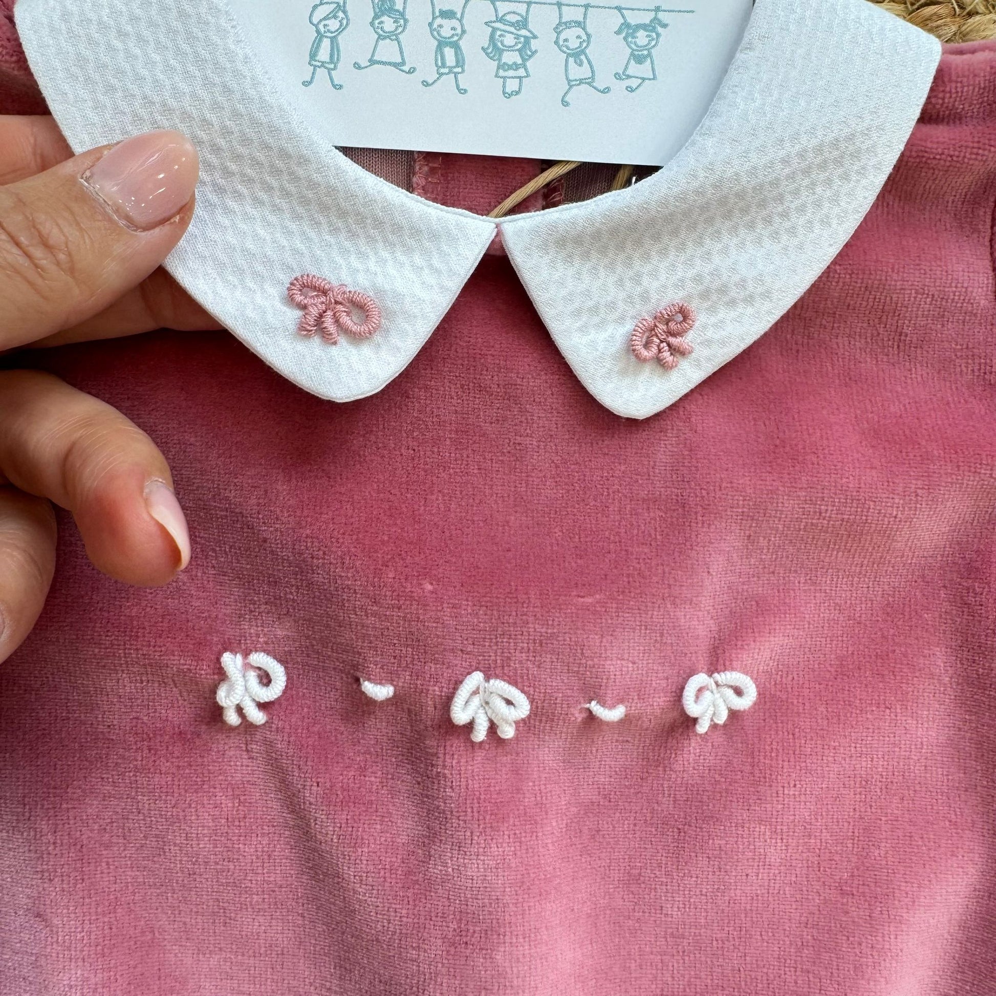 Dettaglio colletto bianco con fiocchi ricamati rosa su tutina neonata in ciniglia