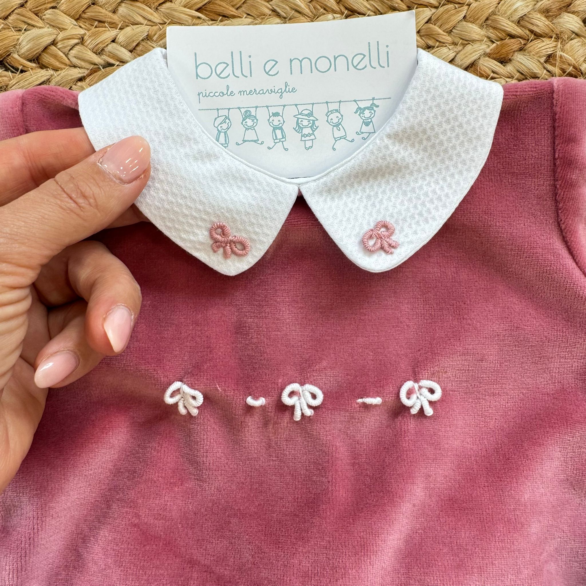 Dettaglio colletto bianco con ricami rosa e fiocchetti sulla tutina in ciniglia