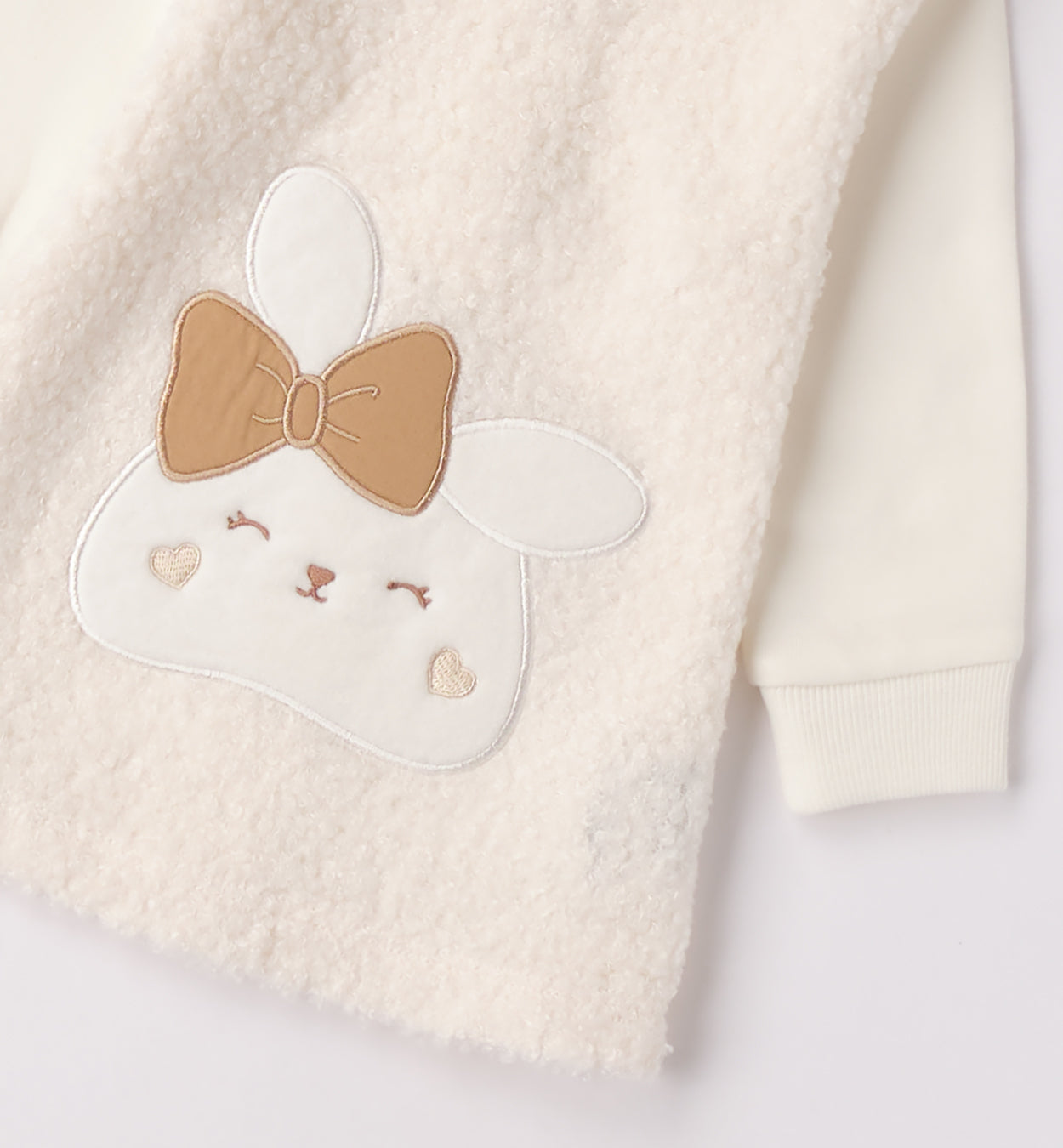 Dettaglio coniglio e fiocco beige su abito bimba panna