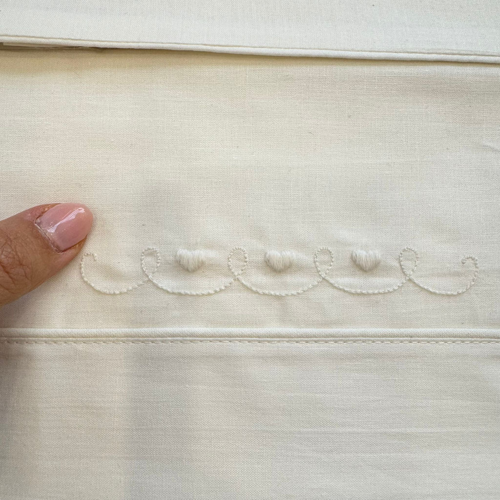 Dettaglio cuori ricamati su lenzuolo in cotone per neonato