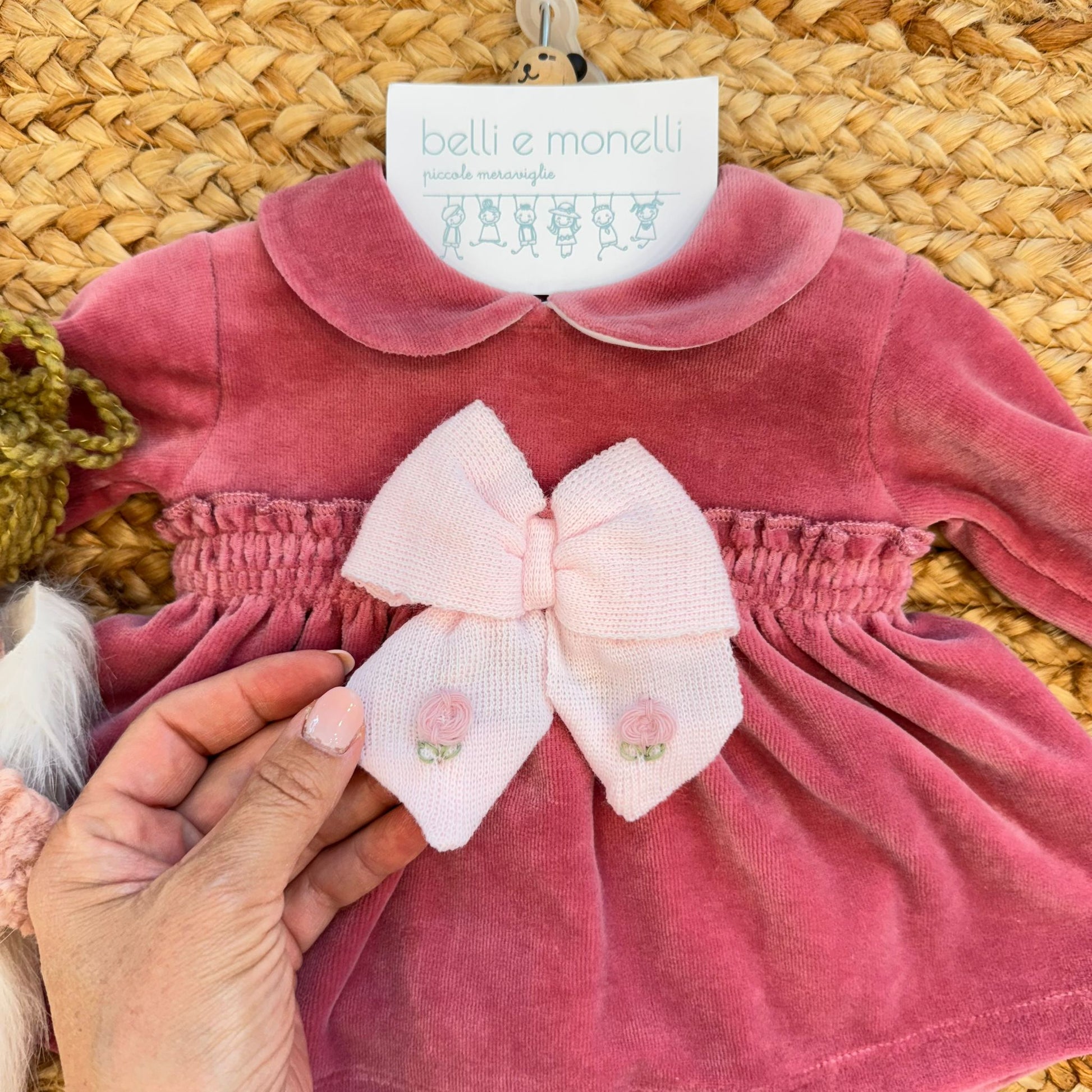 Dettaglio fiocco rosa cipria con ricami floreali su tutina neonata