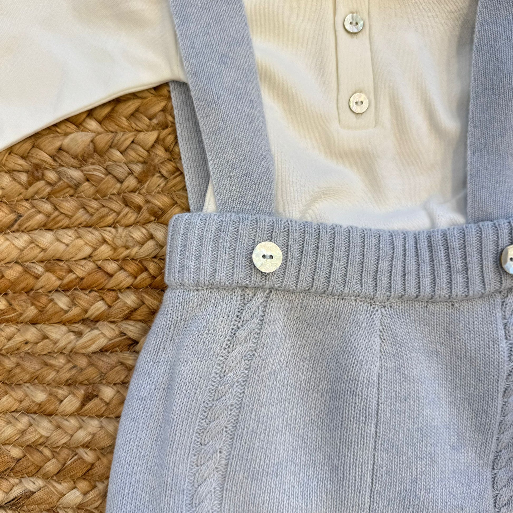 Dettaglio pantaloni azzurri con bretelle lavorate a treccia e bottoni