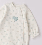 Dettaglio ricamo cuori rosa e beige su tutina neonata in caldo cotone panna.