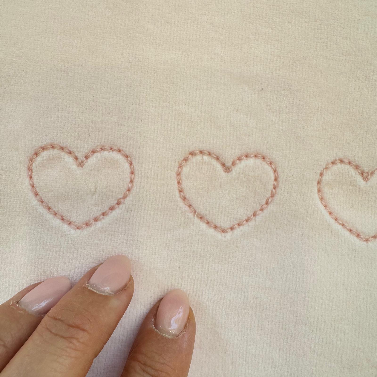 Particolare dei tre cuori rosa ricamati sul cappuccio dell’accappatoio in bambù per neonata.