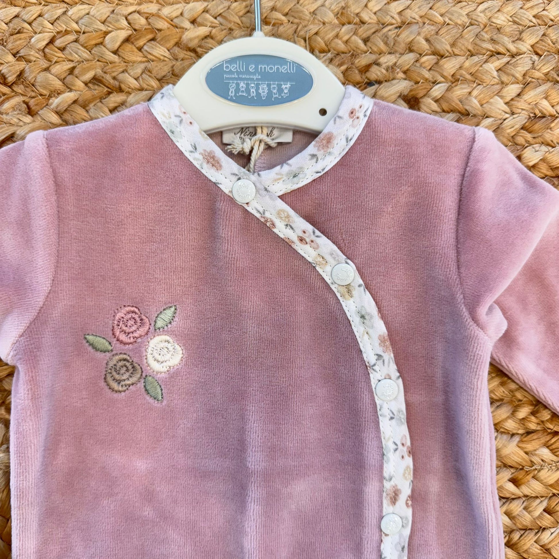 Primo piano ricamo floreale e chiusura laterale tutina neonata ciniglia rosa.