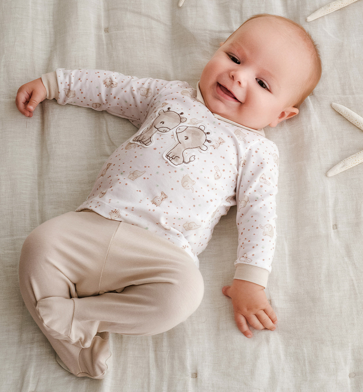 Neonato che indossa una tutina in cotone bianca e beige con ricamo giraffe e fantasia delicata. Completo con piedini, perfetto per il primo corredino e l’uscita clinica.






