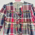 Abito bambina in fantasia tartan scozzese rosso, verde e blu, con maniche lunghe a volant, corpetto arricciato, passamaneria verde e fiocchi frontali.