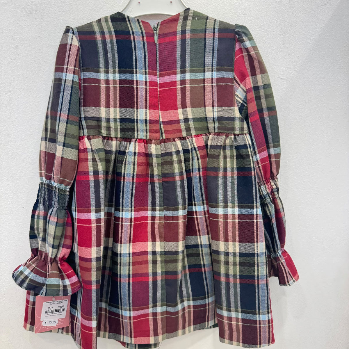 Abito bambina in fantasia tartan scozzese rosso, verde e blu, con maniche lunghe a volant, corpetto arricciato, passamaneria verde e fiocchi frontali.