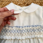Abito battesimo bambina in shantung bianco con smock celeste, maniche a palloncino e colletto tondo.

