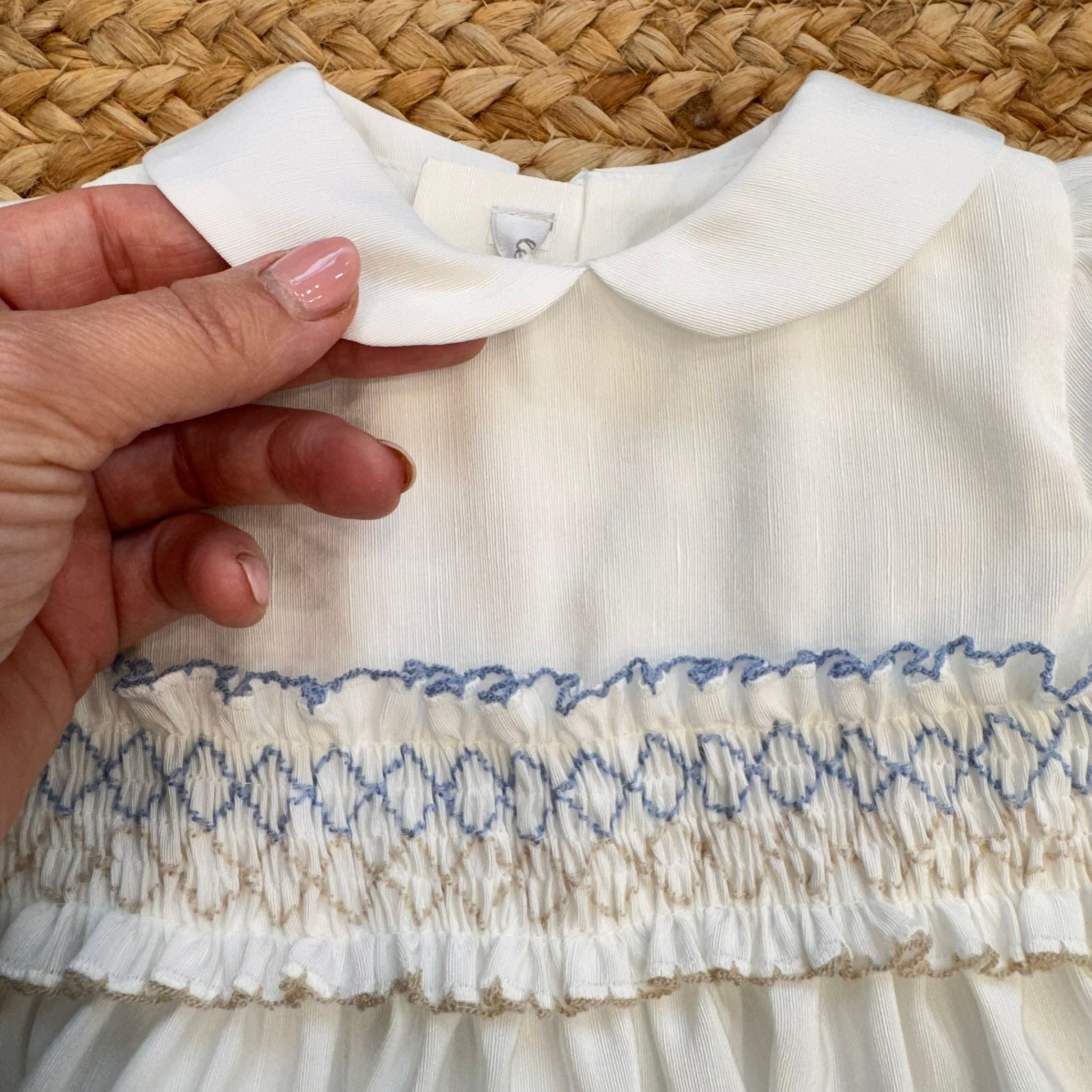 Abito battesimo bambina in shantung bianco con smock celeste, maniche a palloncino e colletto tondo.

