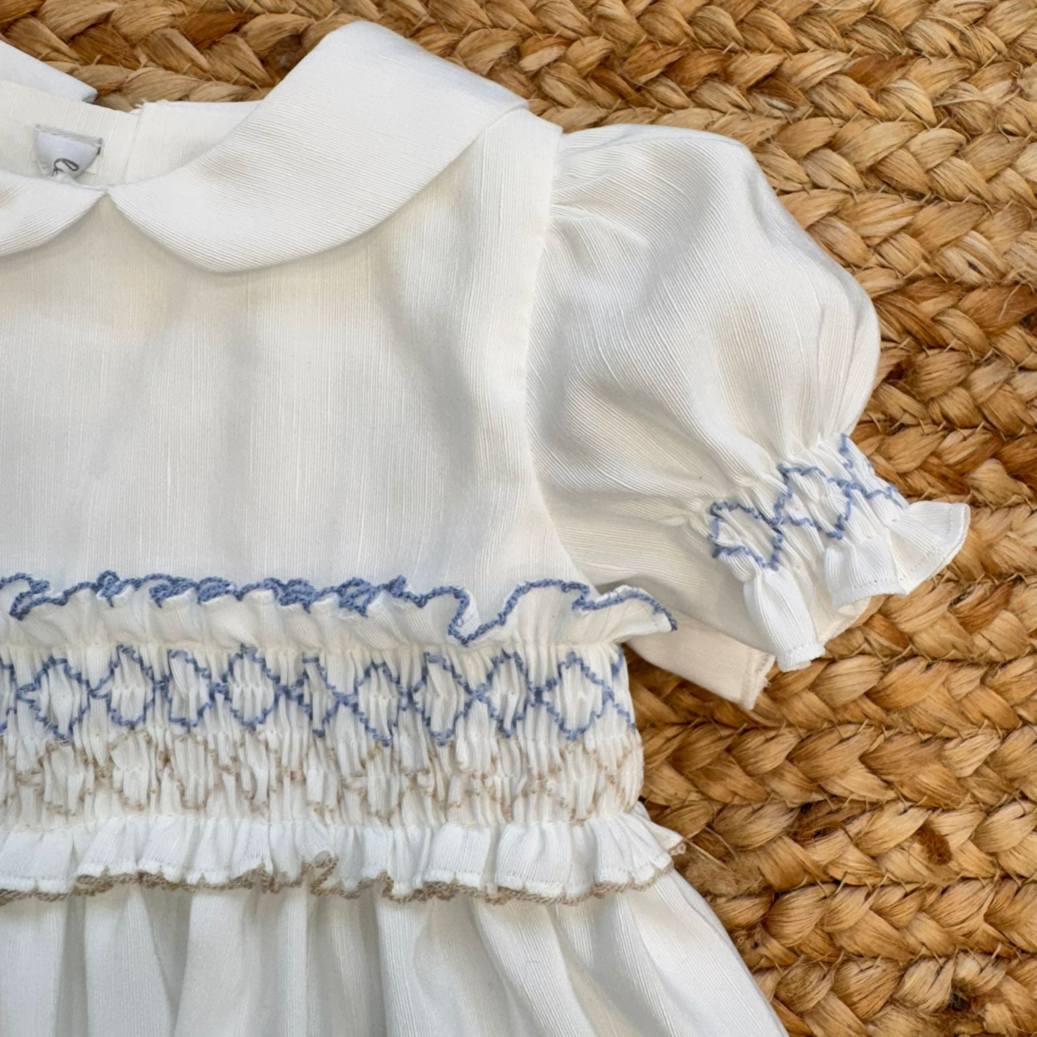 Abito battesimo bambina in shantung bianco con smock celeste, maniche a palloncino e colletto tondo.