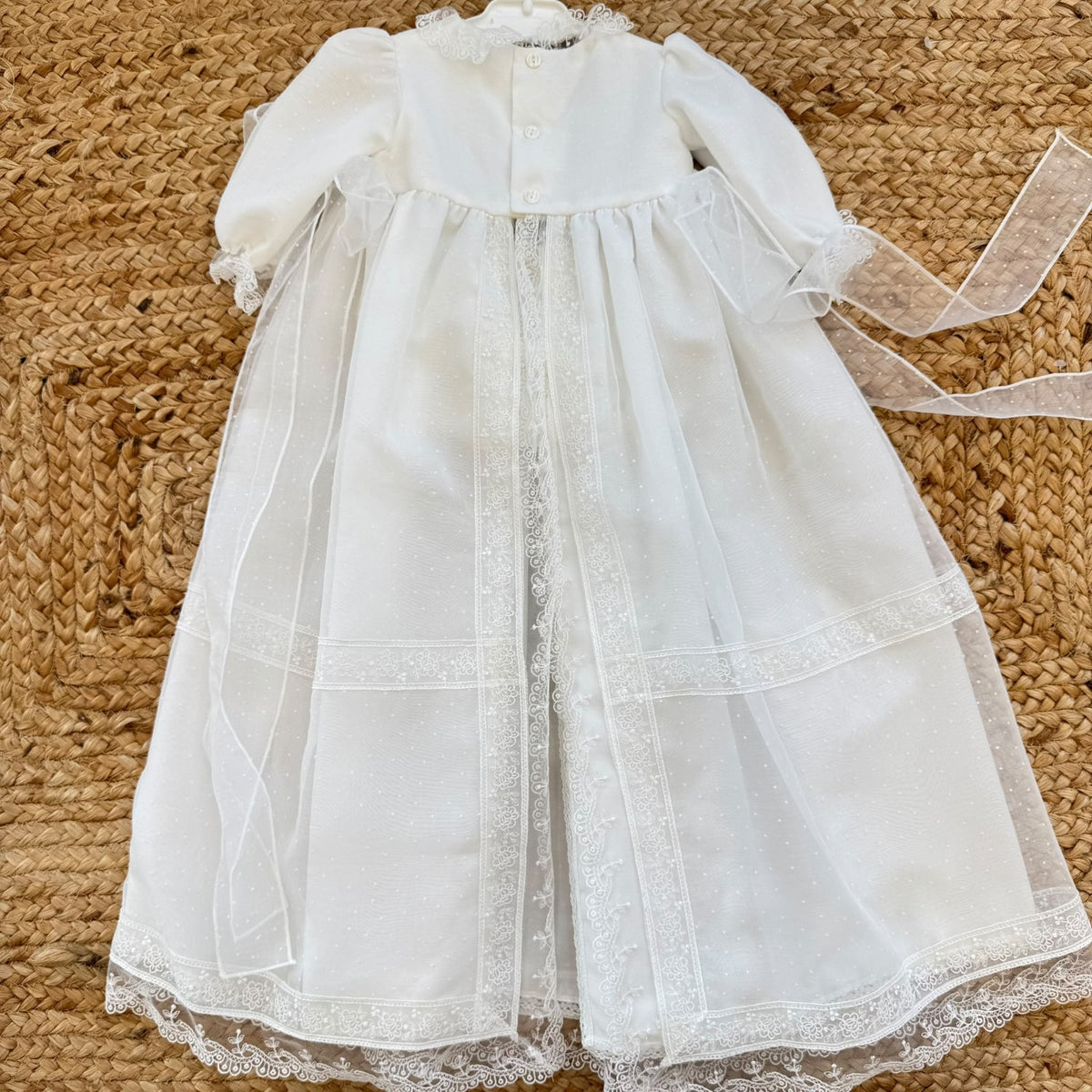 Dettaglio del tessuto a piccoli pois dell'abito battesimo neonata, con ricami floreali bianchi e bordo in pizzo smerlato.