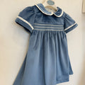 Dettaglio dell'abito bambina in velluto azzurro polvere con lavorazione smock, ricami panna e maniche corte con volant.