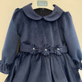Abito elegante bimba blu in velluto con colletto arrotondato, maniche lunghe e tre fiori decorativi sul punto vita.