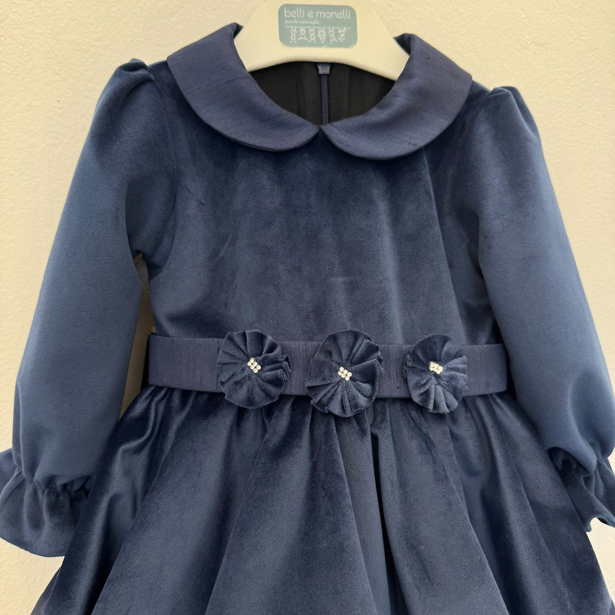 Abito elegante bimba blu in velluto con colletto arrotondato, maniche lunghe e tre fiori decorativi sul punto vita.