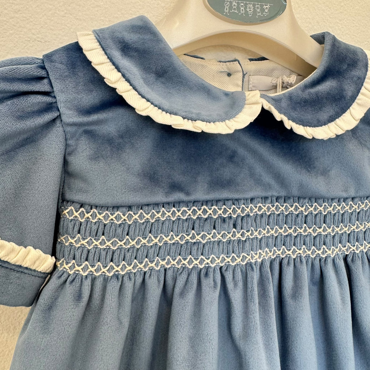 Dettaglio dell'abito bambina in velluto azzurro polvere con lavorazione smock, ricami panna e maniche corte con volant.