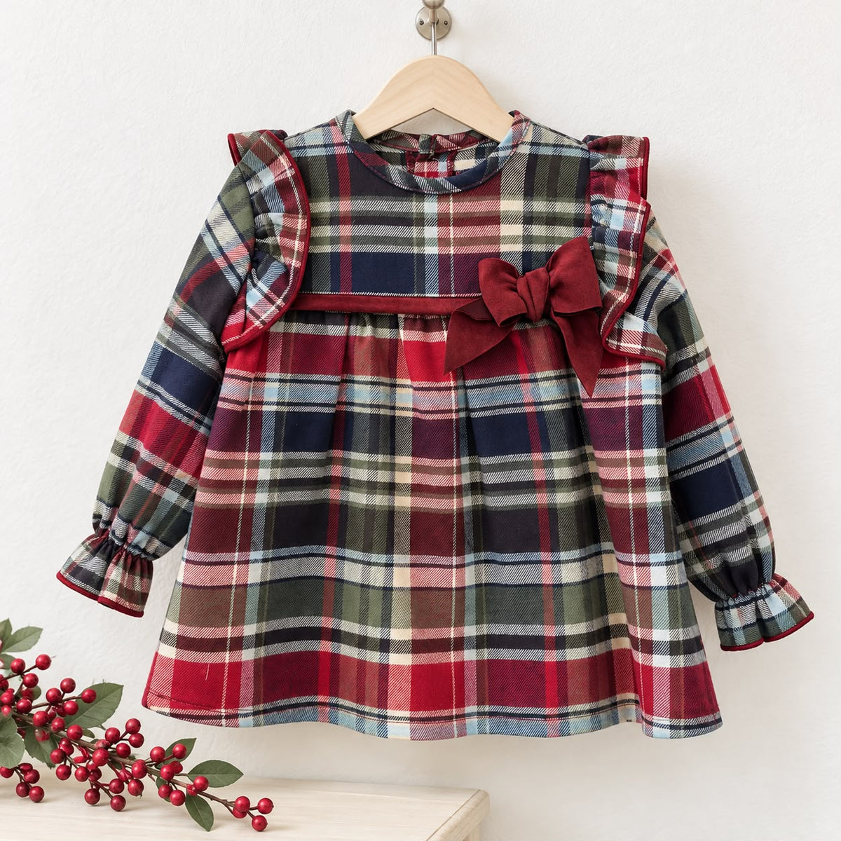 Abito bimba tartan in 100% cotone con fiocco in velluto bordeaux, ruches sulle spalle e gonna arricciata. Elegante per Natale e occasioni speciali.