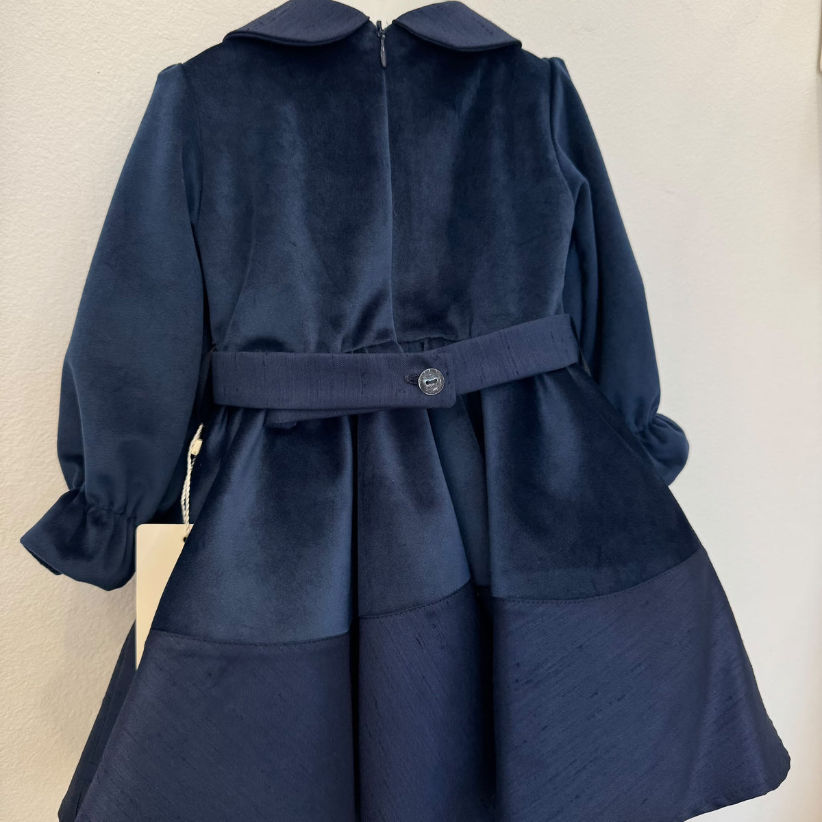 Abito elegante bimba blu in velluto con colletto arrotondato, maniche lunghe e tre fiori decorativi sul punto vita.