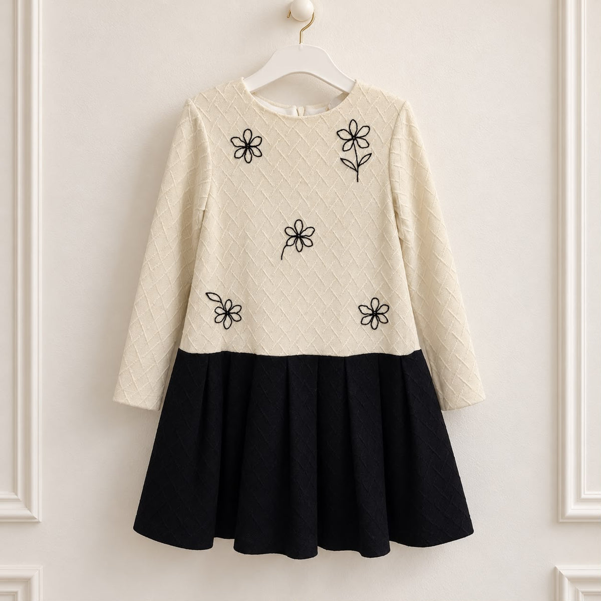 Abito elegante bambina panna e nero con fiori ricamati neri, corpetto lavorato a rombi, maniche lunghe e gonna nera a pieghe.
