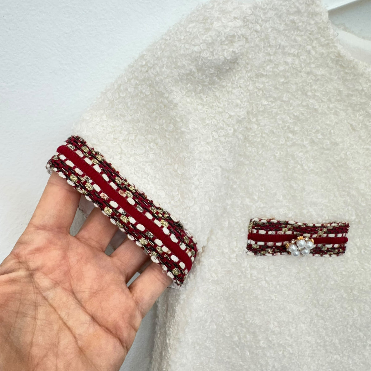 Dettaglio abito elegante bambina panna bouclé con passamaneria bordeaux e decorazioni di perline