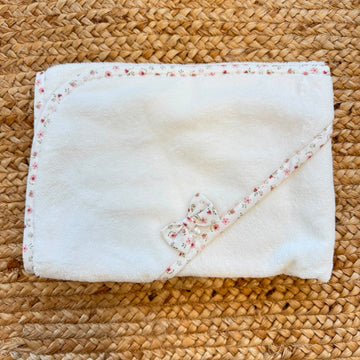 : Accappatoio neonata in spugna di cotone bianco con cappuccio, bordo floreale rosa e fiocco decorativo.