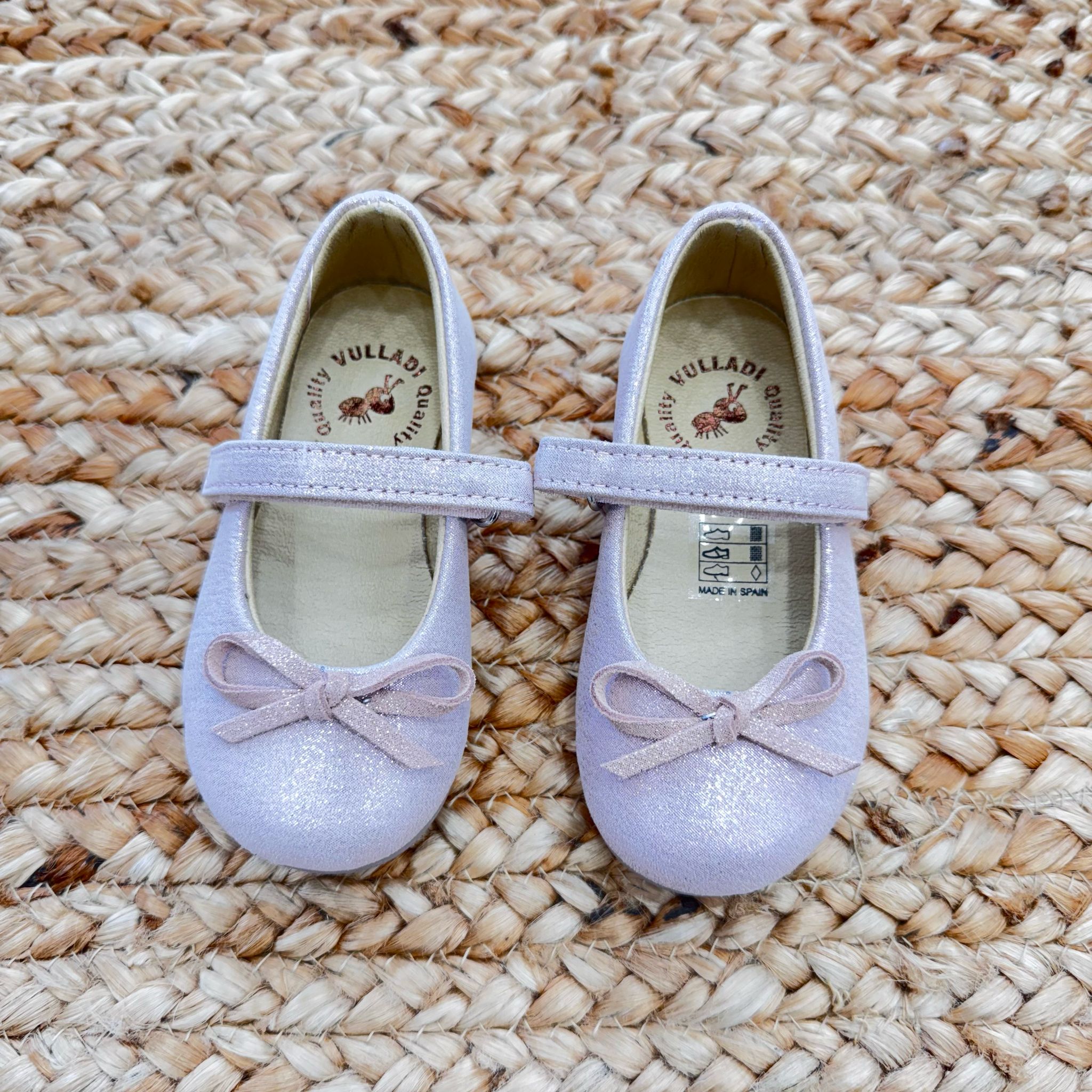 Ballerine taupe in camoscio per bambina con cinturino e fiocco decorativo, perfette per cerimonie ed eventi speciali.