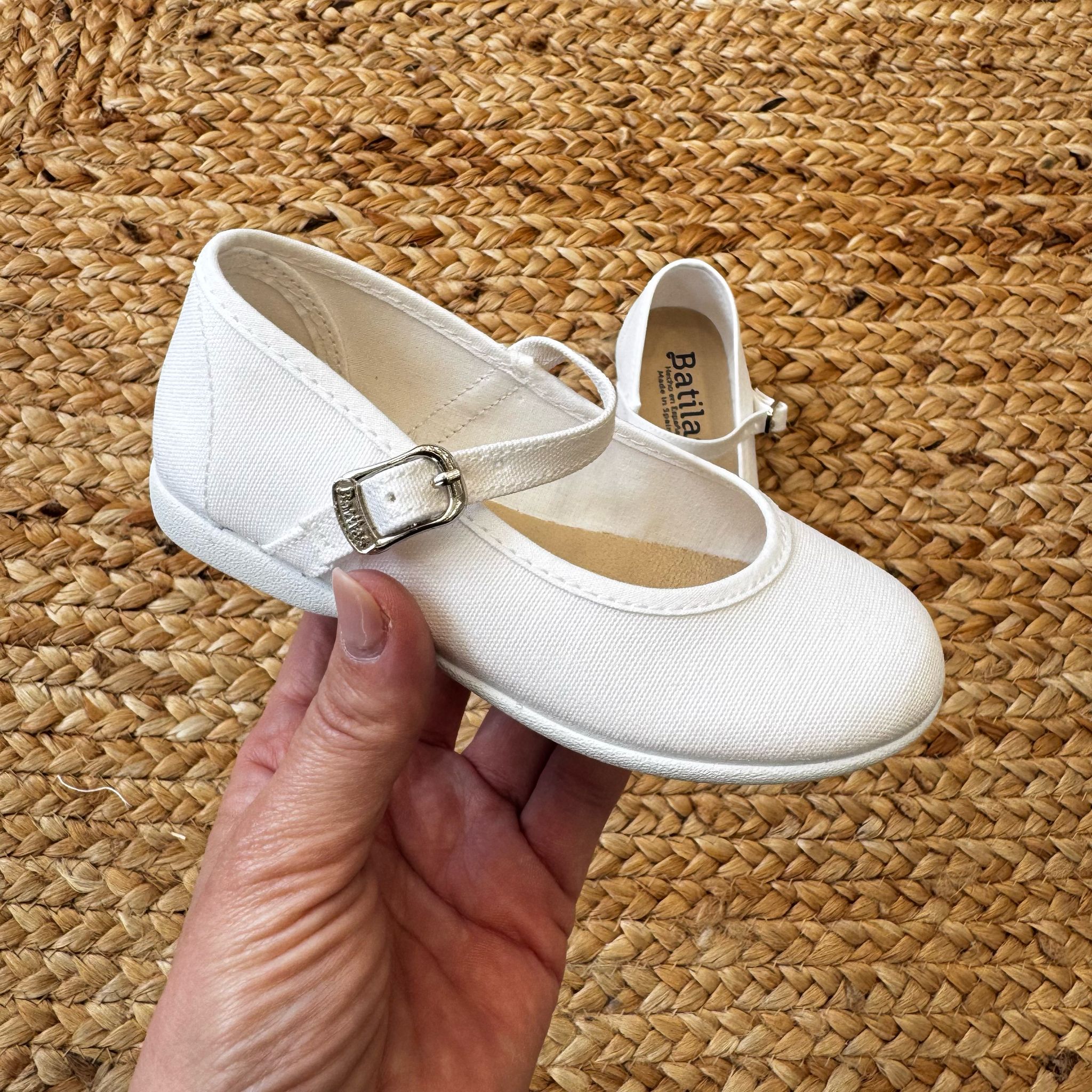 Ballerine bianche in tessuto per bambina con cinturino e fibbia laterale, ideali per cerimonie e occasioni speciali.
