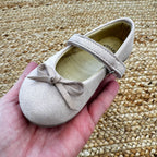 Ballerine taupe in camoscio per bambina con cinturino e fiocco decorativo, perfette per cerimonie ed eventi speciali.