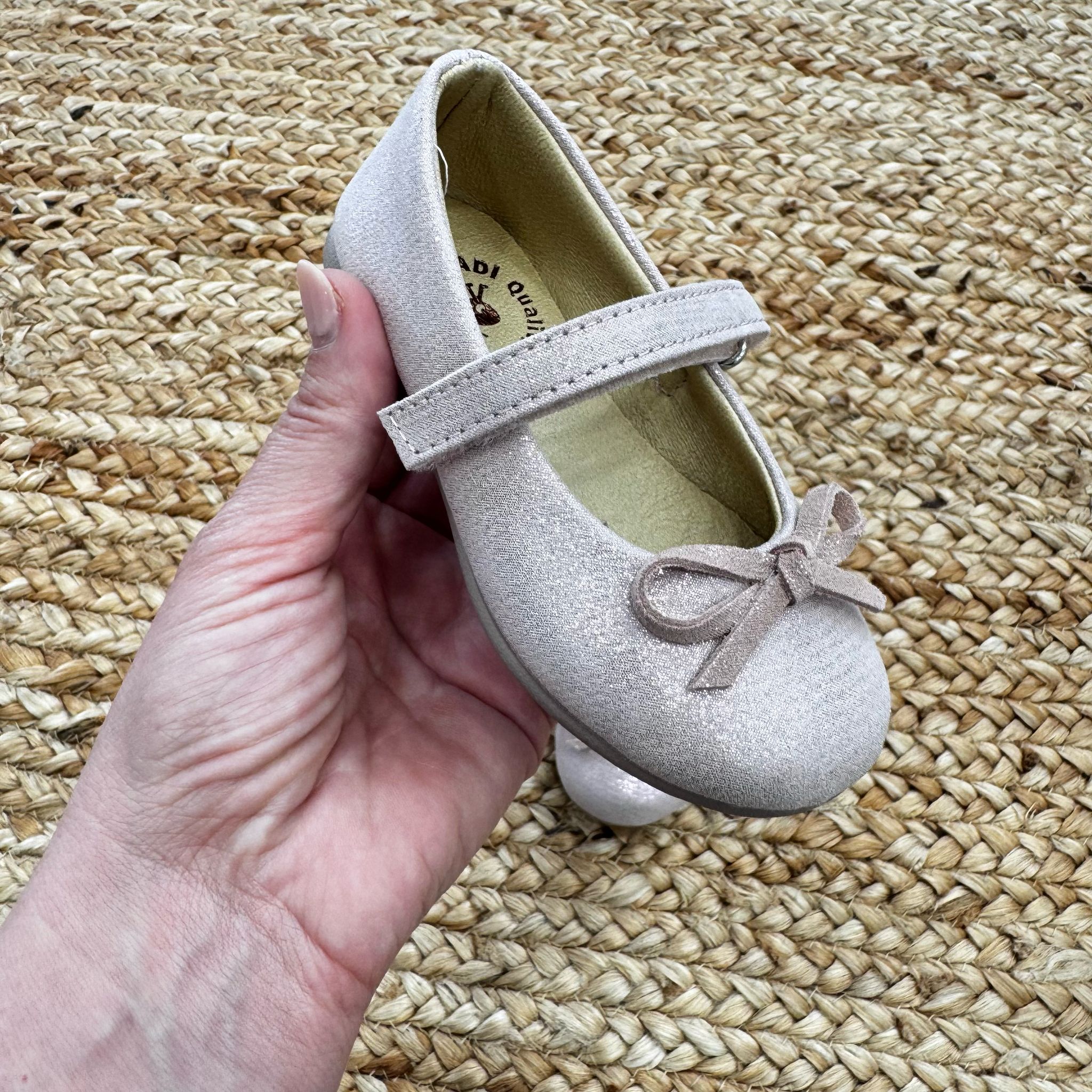 Ballerine taupe in camoscio per bambina con cinturino e fiocco decorativo, perfette per cerimonie ed eventi speciali.