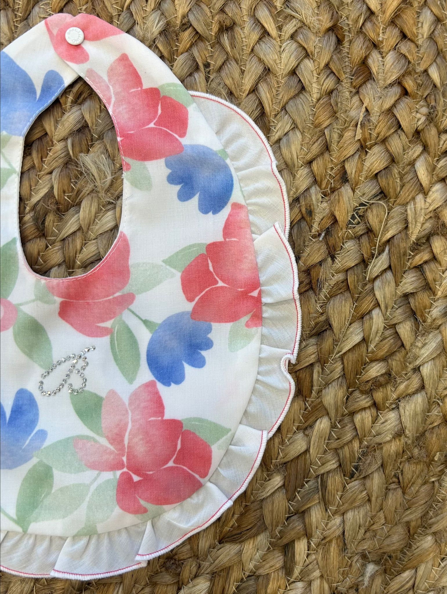 Bavaglino neonata in cotone con fiori e farfalle acquerello, balza arricciata e strass decorativi a forma di B.


