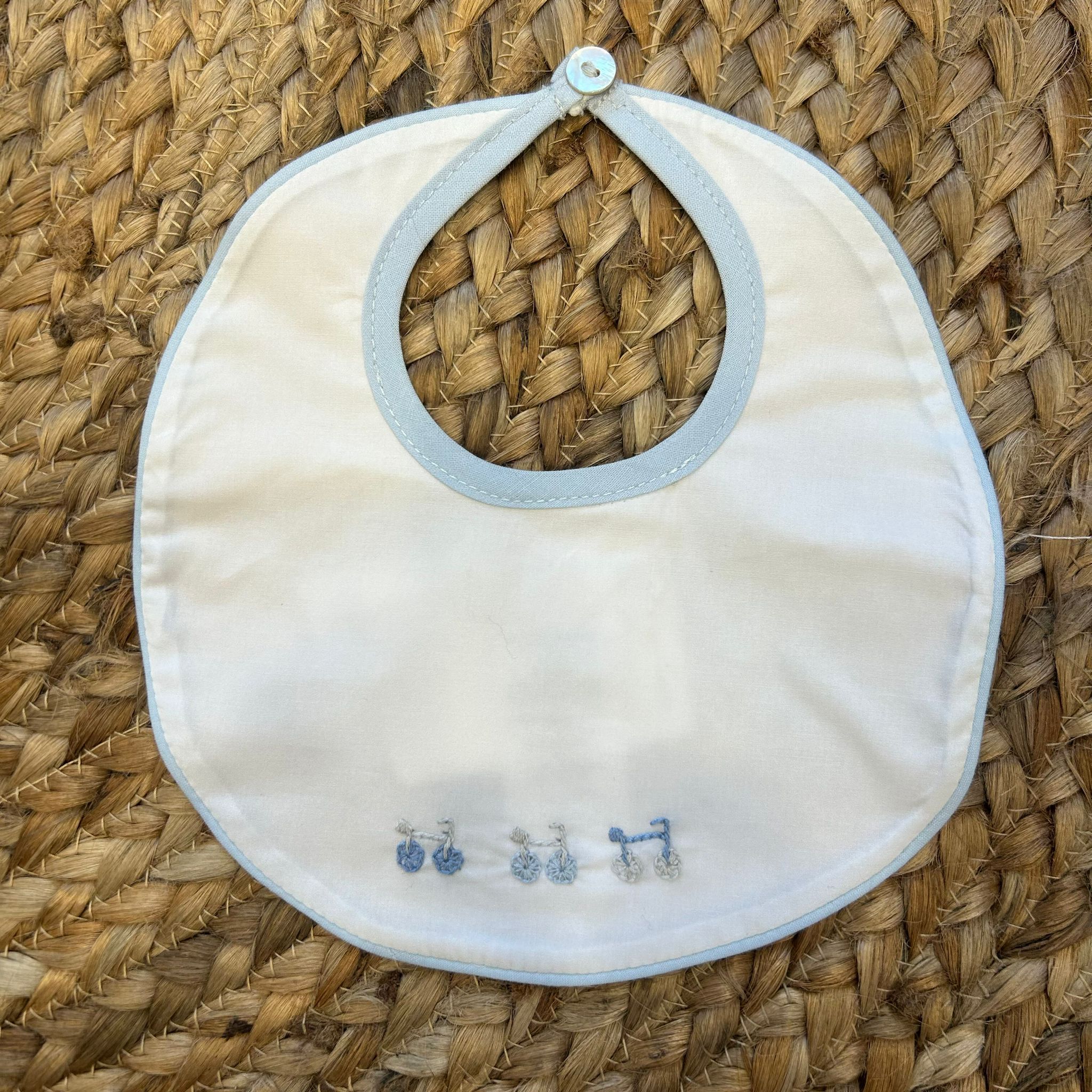 Bavaglino neonato con bordino azzurro e ricamo bici in cotone bianco.

