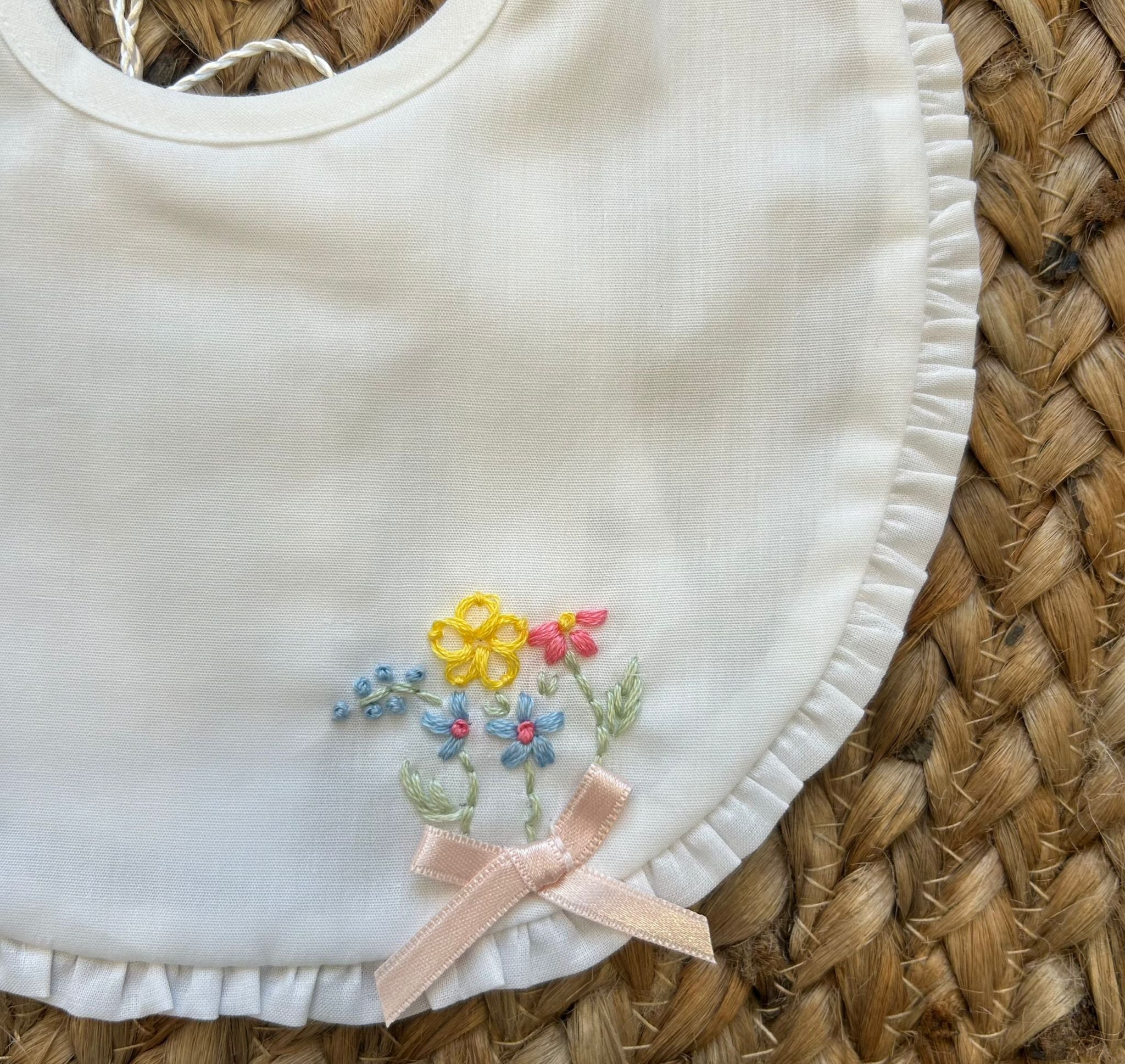 Bavaglino bianco con ricami floreali e fiocco rosa cipria