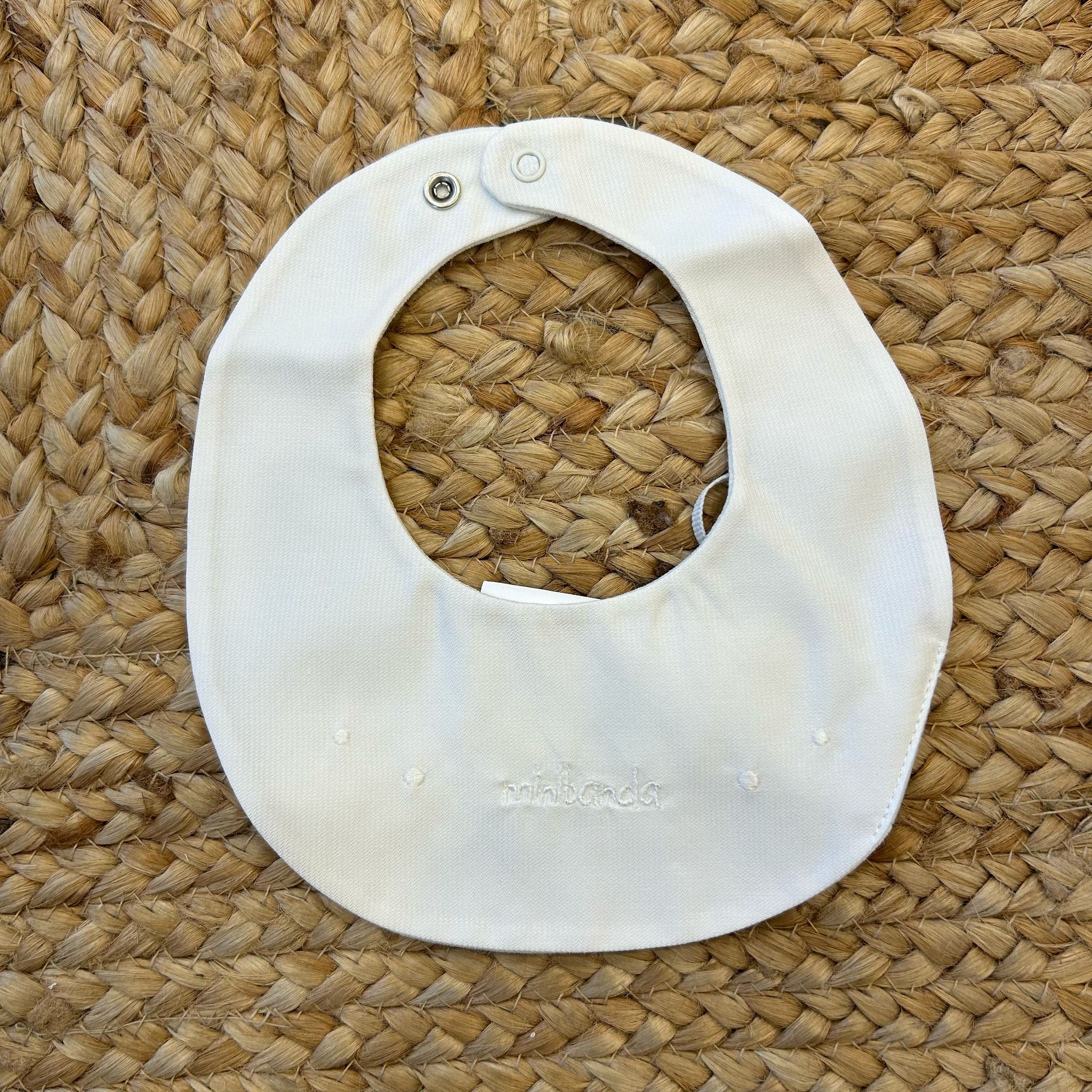 Bavaglino neonato panna con ricamo bianco “ninnanda” e chiusura a clip.

