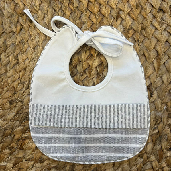 Bavaglino neonato in cotone bianco con fasce a righe grigie in lino e chiusura con fiocco.