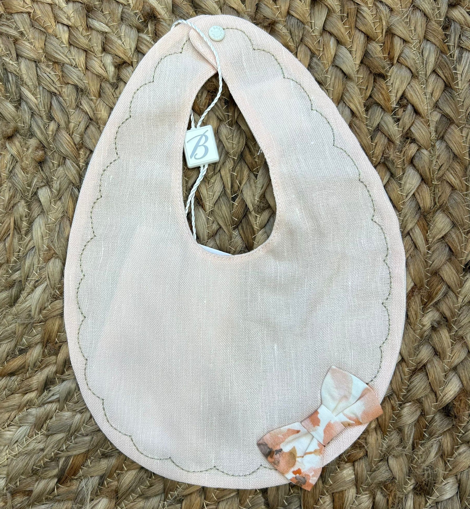 Bavaglino neonata rosa pesca in lino con bordo smerlato e fiocchetto fantasia.