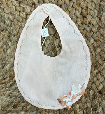 Bavaglino neonata rosa pesca in lino con bordo smerlato e fiocchetto fantasia.